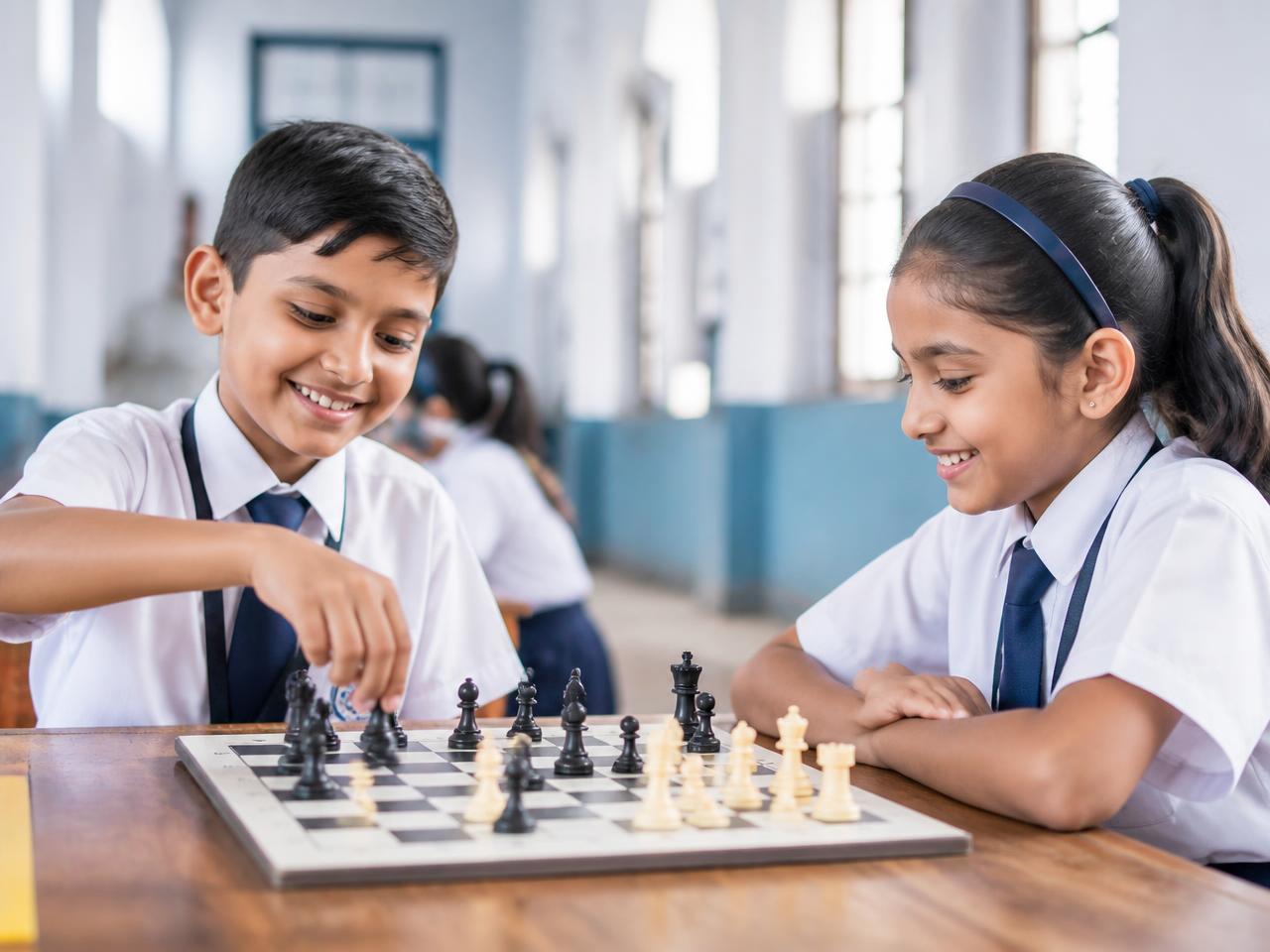 Two school children smiling while playing chess in a school hall